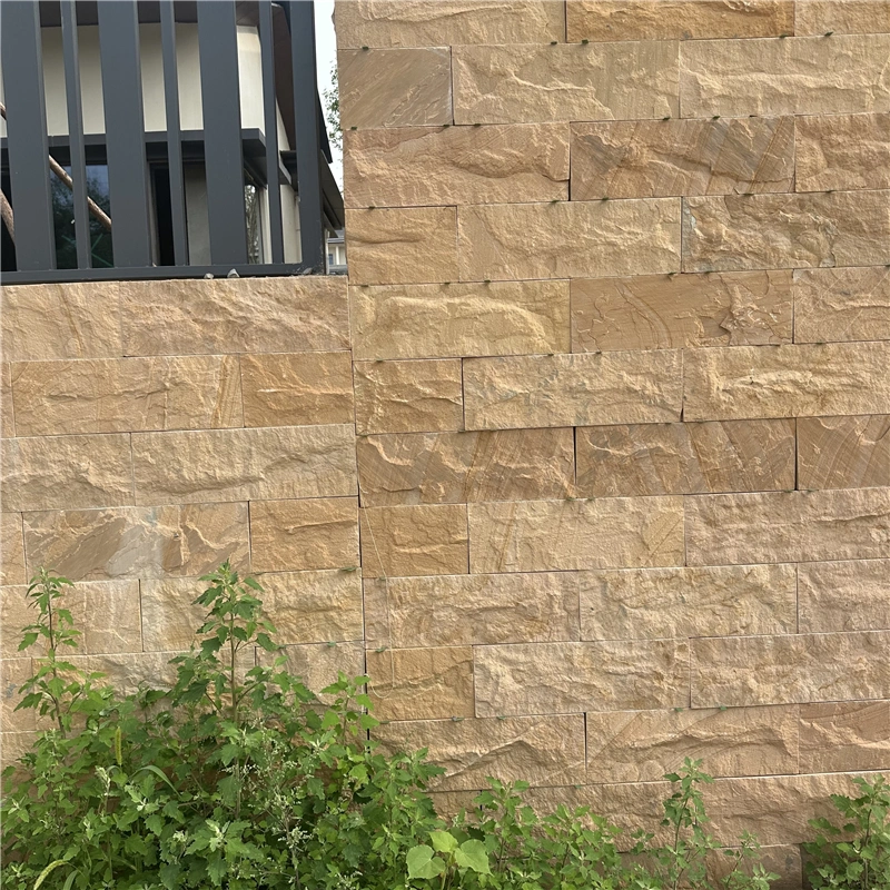 Yellow sandstone rock‑face cladding on residential garden retaining wall with surrounding green plants