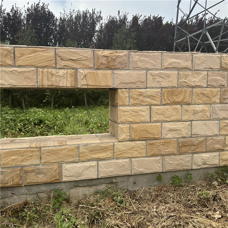 Yellow sandstone rock‑face cladding on outdoor landscape wall with hollow window opening, under‑construction site view